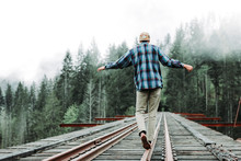Young Man Balancing On Railroad Tracks Over Bridge In Foggy Forest