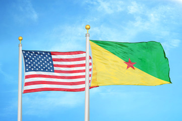 United States and French Guiana two flags on flagpoles and blue cloudy sky