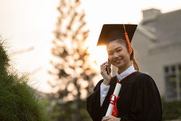 Happy graduated young woman in cap and gown talking with parent in mobile phone and looking certificated in hand so proud happiness in Commencement day,Congratulation of student in graduation day