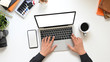 © Prathankarnpap - Top view Creative man's hands typing on computer laptop with white blank screen that putting on white working table surrounded with coffee cup, empty screen smartphone and accessories.