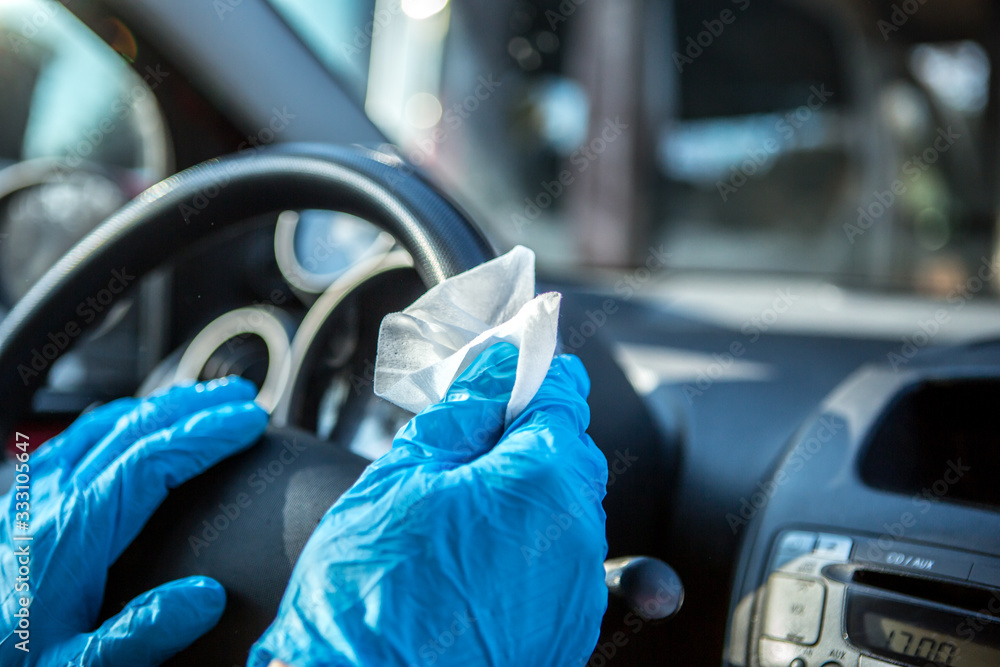 Coronavirus Epidemic Outbreak. Close-up of hand in protective glove using wet wipe to disinfect car steering wheel.  - obrazy, fototapety, plakaty 