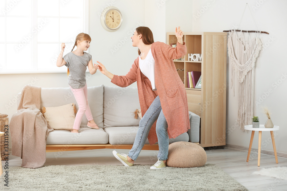 Happy mother and her little daughter dancing at home