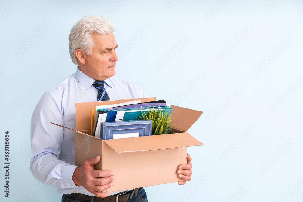 Sad fired mature man with personal stuff on color background