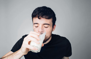 Young man isolated over background. Male person in casual style drink milk or sour milk from glass. Thirsty. Alone in studio. Drinking with pleasure.