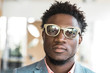 © Mangostar - Serious trendy guy posing indoors. Closeup of young African American man wearing stylish glasses, bright shirt and jacket, looking at camera. Fashion or male portrait concept