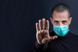 Ragazzo rasato indossa una mascherina chirurgica verde e indica con le mani il segno di stop, isolato su sfondo nero