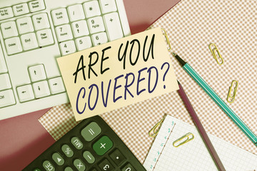 Handwriting text Are You Covered Question. Conceptual photo asking showing if they had insurance in work or life Note paper stick to computer keyboard near colored gift wrap sheet on table