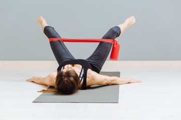 Wall Mural - Determined to win. Modern young woman in sport clothing crouching using resistance band while exercising in the gym