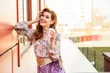 © Вячеслав Чичаев - Photo in bright weather of a fashionable glamorous beautiful woman with long hair against the background of the spring city in the sun. Model is standing outdoors with a cup of coffee in her hands.