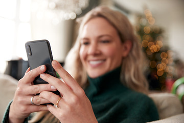 Wall Mural - Close Up Of Woman Relaxing On Sofa At Home At Christmas Using Mobile Phone