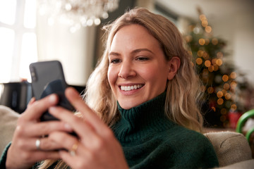 Wall Mural - Close Up Of Woman Relaxing On Sofa At Home At Christmas Using Mobile Phone