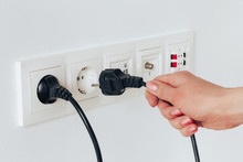 A Female Hand Is Pulling An Electrical Cord Plugged Into A Socket