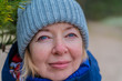 Cheerful mature woman smiling. Wearing blue knitted hat. Outdoors cold weather portrait. Face close up.