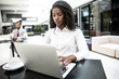 © Mangostar - Serious young businesswoman working on laptop while drinking coffee in office lobby. Businessman in formal suit using tablet in background. Co-working space concept
