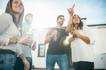 Wall Mural - Positive friends drinking beer and waiting someone on outdoor terrace. Young men and women in casual meeting outside. Friendly party or communication concept