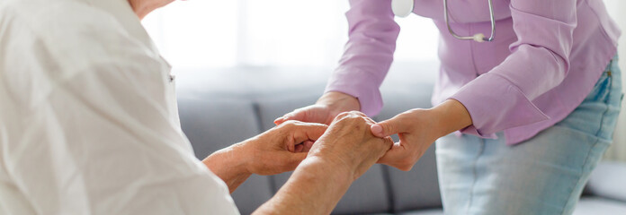 Young doctor holding hand of elderly woman on light background