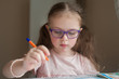 © Kiryakova Anna - Happy pretty child girls sitting at the table and writes. Educational activities at home. Distance learning. Girl with glasses. Vision problems