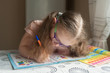 © Kiryakova Anna - Happy pretty child girls sitting at the table and writes. Educational activities at home. Distance learning. Girl with glasses. Vision problems