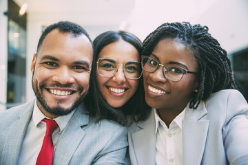 Happy joyful diverse business colleagues taking selfie. Self portrait of young African American and Latin women and Caucasian man, wearing formal suits and smiling. Happy team concept