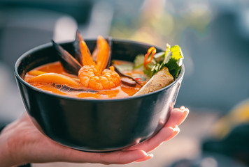 Poster - pan asian food. woman hands holding Tom Yam soup in black bowl