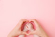 Heart shape created from young mother hands. Infant arms in middle. Light pink table background. Pastel color. Lovely emotional, sentimental moment. Empty place for text, quote or sayings. Top view.
