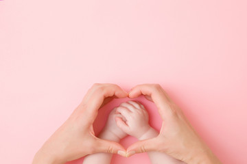 heart shape created from young mother hands. infant arms in middle. light pink table background. pas
