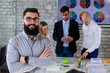 © Andrej - Confident successful business man posing in front of a team of young business people or designers discussing new projects and new business ideas in  modern office. Startup concept.