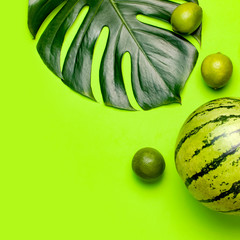 Ripe watermelon berry, whole limes, tropical leaf monstera on green background top view flat lay. Green Striped Whole Watermelon. Summer bright background. Creative Minimal fruit concept