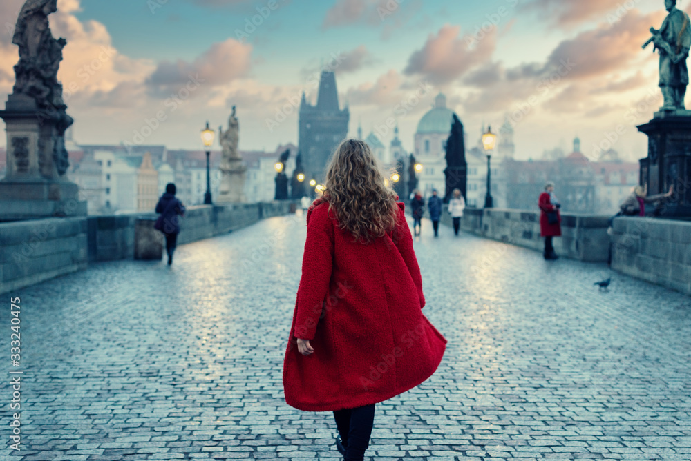 Obraz na płótnie Woman in red coat walking on The Charles Bridge in Prague during the atmospheric sunset in winter w salonie