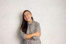 Shy Smiling Woman With Stylish Haircut With Arms Crossed. Happy Girl On White Brick Wall