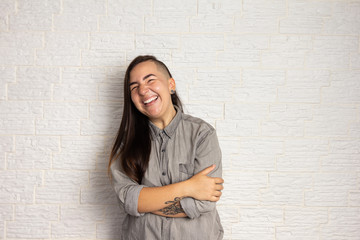 Shy smiling woman with stylish haircut with arms crossed. Happy girl on white brick wall