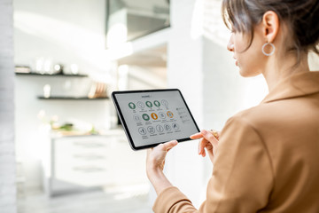 Woman controlling smart home devices using a digital tablet with launched application in the white living room. Smart home concept