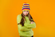 © Tina kids photo - Happy teen girl in green sweater and multi-colored knitted hat on a yellow background