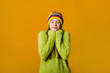 © Tina kids photo - Happy teen girl in green sweater and multi-colored knitted hat on a yellow background