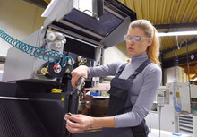 A Young Woman Works As A Computerized  Numerical Control Technician. She Is Seen At Her Workplace Wearing A Blue Overall. 