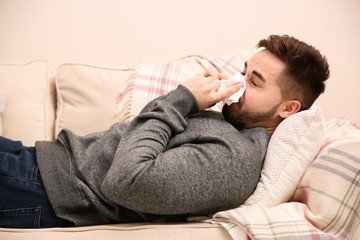 Wall Mural - Sick young man sneezing at home. Influenza virus