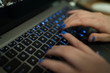 Kobieta pisze maila na klawiaturze laptopa (komputera). Przyciski mają niebieskie podświetlenie