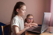 © Kiryakova Anna - Two girls, the oldest and the youngest, are engaged at a table on a laptop. Little sister with glasses.