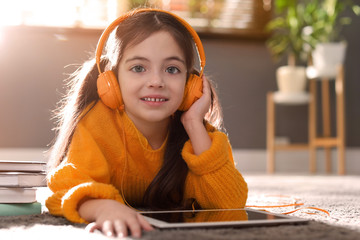 Sticker - Cute little girl with headphones wearing orange knitted sweater at home