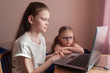 © Kiryakova Anna - Two girls, the oldest and the youngest, are engaged at a table on a laptop. Little sister with glasses.
