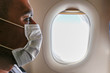 Portrait of adult man on wearing disposable raspiratory face mask for coronavirus protection, flying home on the evacuation plane, looking at porthole. Close up, copy space, background.