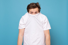 Shy Caucasian Man Hiding Behind His White Shirt Being Afraid Of Coronavirus.