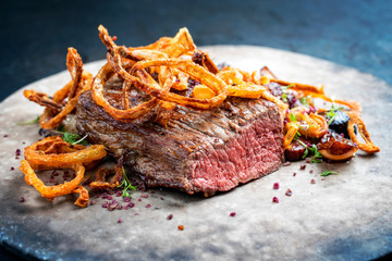 Wall Mural - Traditional dry aged sliced roast beef with fried onion rings and potatoes served as closeup on a modern design plate