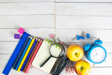 Various office stationery, notepad, clock, pencils, ooh, glasses, pen and two fresh apples on a white wooden table. Top view with copy space. Concept of office, education, workplace, school