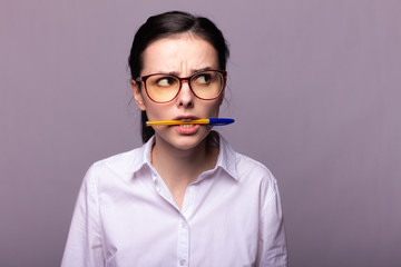  girl in a white shirt and glasses holds a pen with her mouth