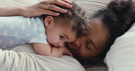 Wall Mural - loving african young mommy hugging soothing adorable sweet baby boy lying in bed. smiling caring mix