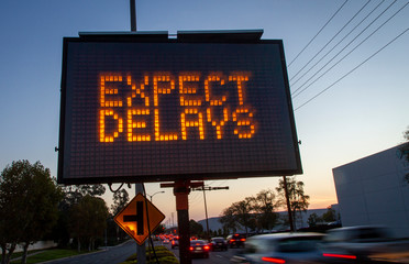 Electrionic traffic sign stating Expect Delays with blurred traffic at sunset
