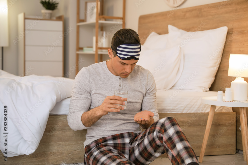 Young man taking pills for insomnia in bedroom