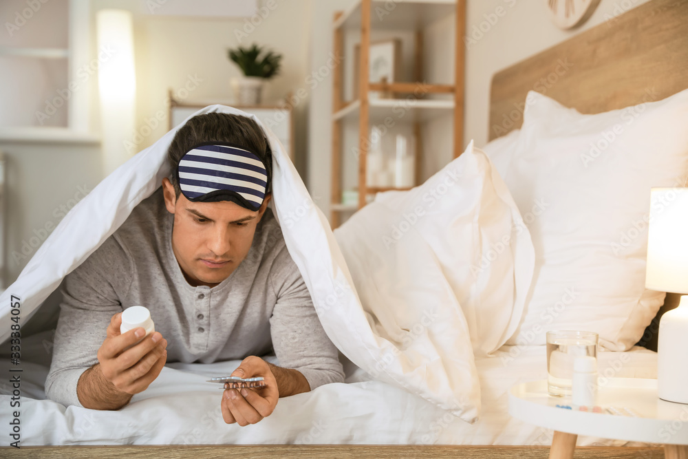 Young man with pills for insomnia in bedroom