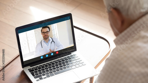Focus on computer screen with confident happy male family doctor general practitioner consulting giving advices to older mature worried man patient with sickness symptoms online via video call..